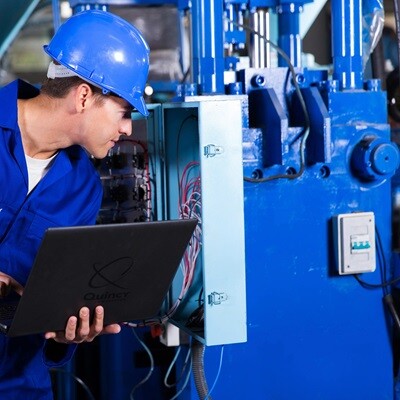 Worker examining industrial machinery with a laptop.