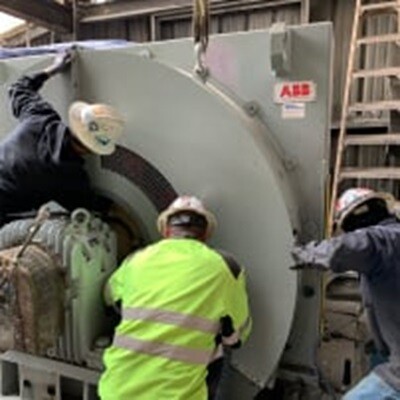 Three workers in safety gear adjusting a large industrial machine component.