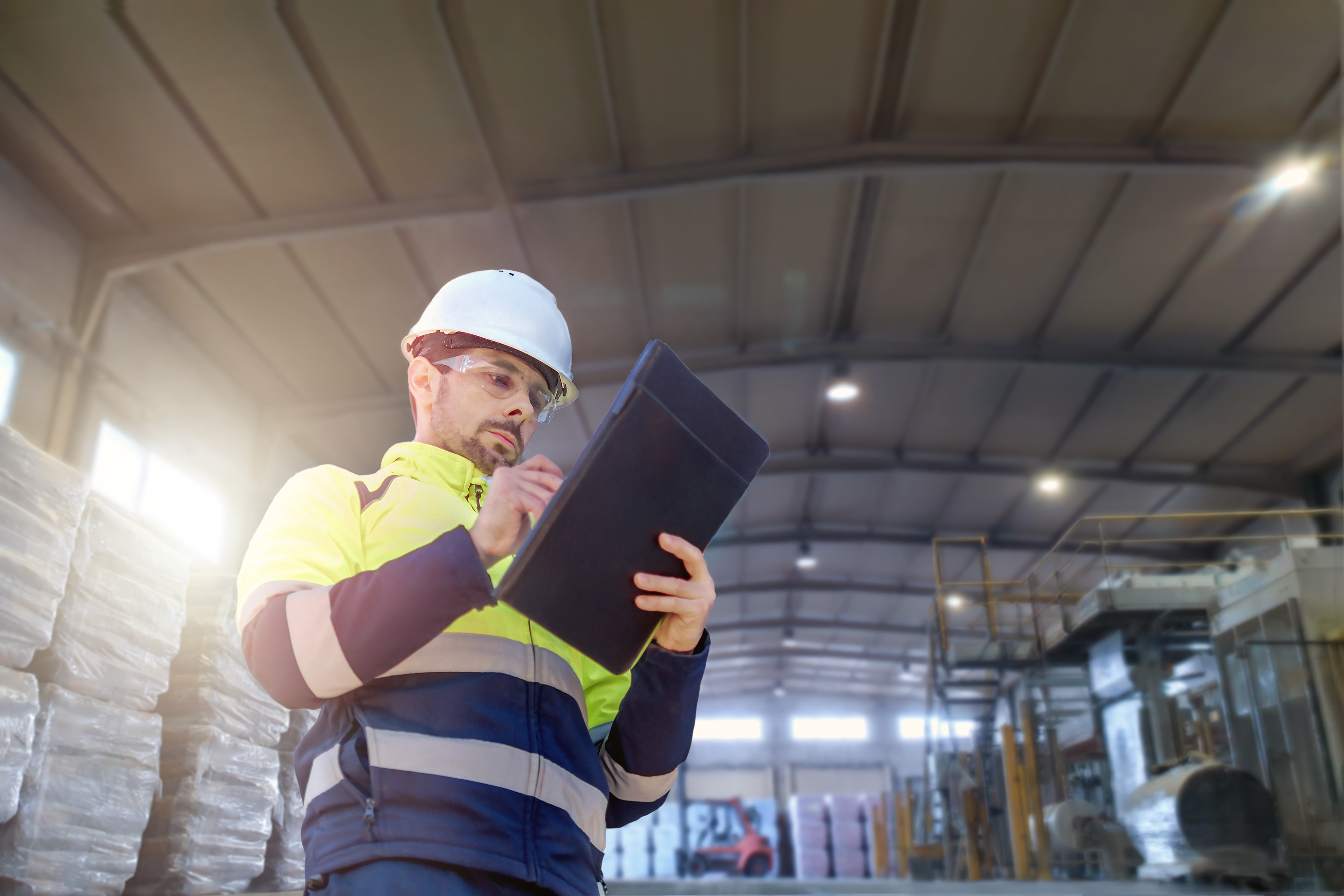 man in a hard hat and safety vest with a clipboard in a warehouse